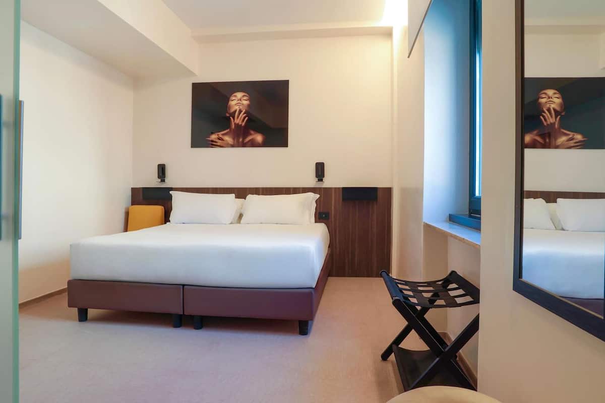 A bedroom with a bed, a chair, a painting, and a mirror.