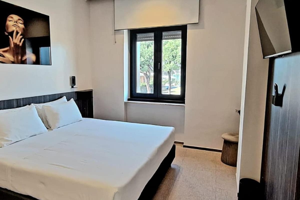 A bedroom with a bed, a wall-mounted mirror, a window, and a door.