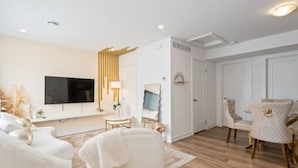 A modern living room with a flat-screen TV, a white sofa, a dining area with a table and chairs, and a wooden floor. - Casa Nova Niagara- New home with a chic and Style (Niagara Falls)
