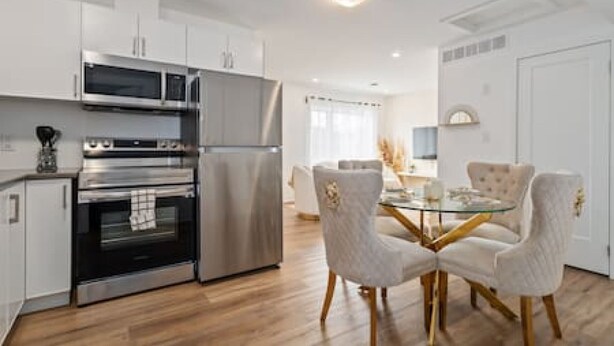 A modern kitchen with stainless steel appliances, a dining area with a glass table and upholstered chairs, and a white door. - Casa Nova Niagara- New home with a chic and Style (Niagara Falls)