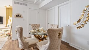 A dining area with a glass table surrounded by upholstered chairs, white walls, and a decorative gold leaf wall art piece. - Casa Nova Niagara- New home with a chic and Style (Niagara Falls)