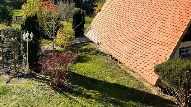 A house with a sloped red-tiled roof, surrounded by a well-maintained garden with various shrubs and a small pond. - Newly built apartment with lake view-Teupitzer Str.9 Tornow (Teupitz)