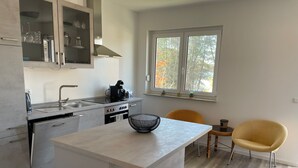 A modern kitchen with a central island, a sink, a stove, and a window with a view of trees. - Newly built apartment with lake view-Teupitzer Str.9 Tornow (Teupitz)