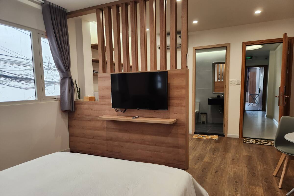 Habitación de hotel con cama, televisor de pared, paneles de madera, ventana con cortinas y vistas al exterior.