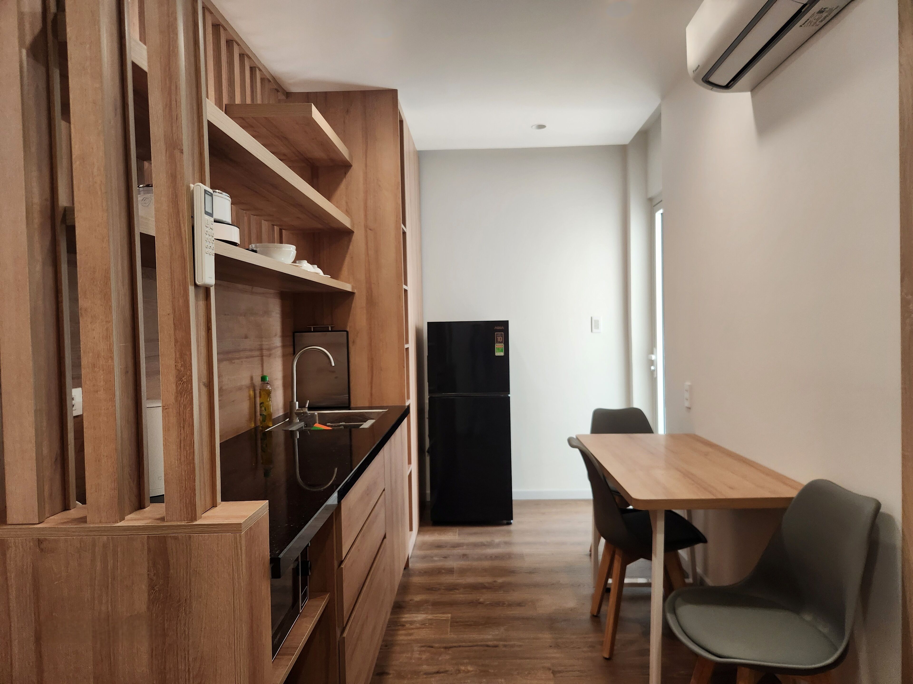 A compact kitchen with wooden cabinetry, a black refrigerator, a sink, and a dining area with a table and chairs.