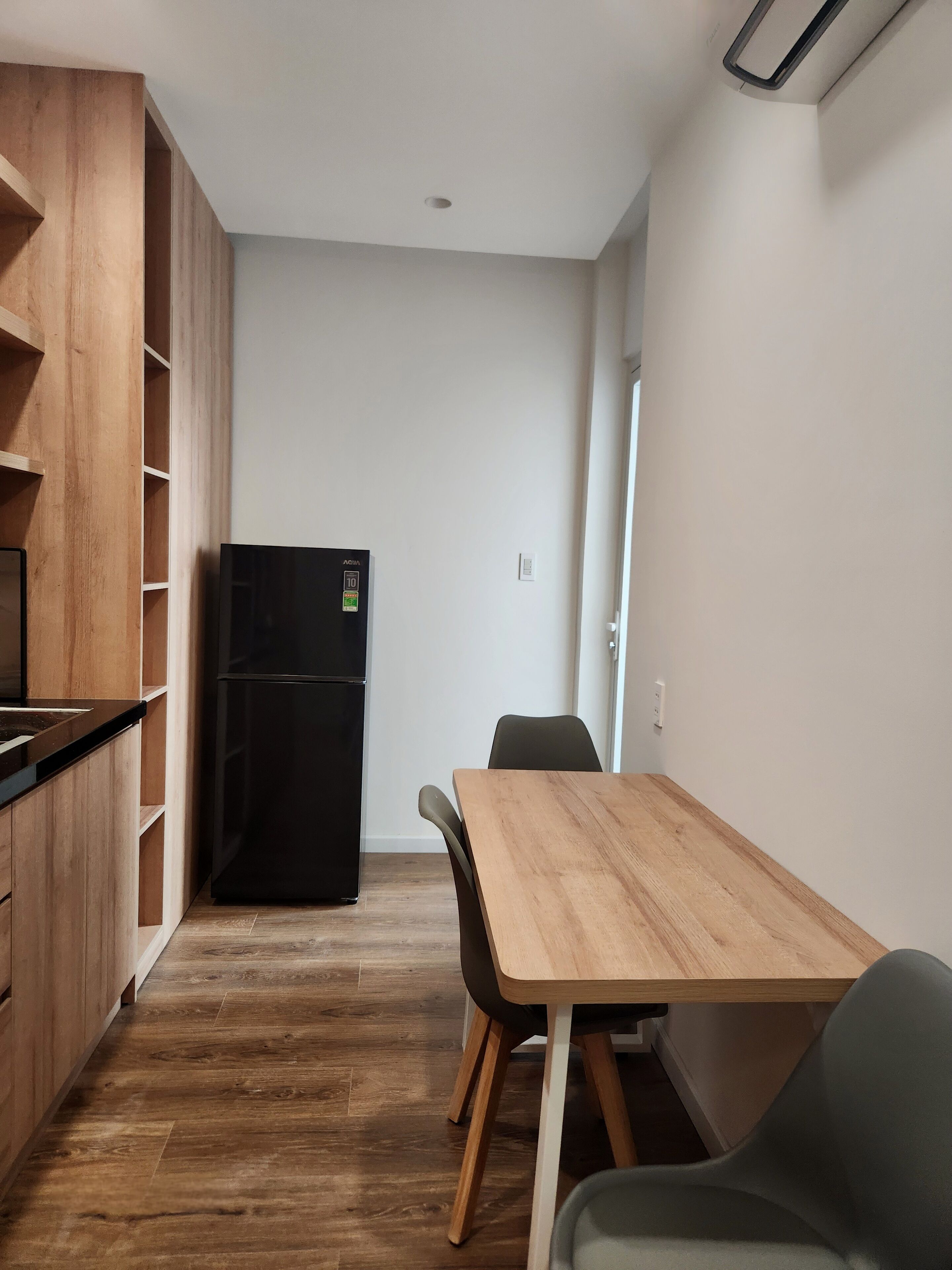 Una cucina compatta con mobili in legno, un frigorifero nero e un'area pranzo con tavolo e due sedie.