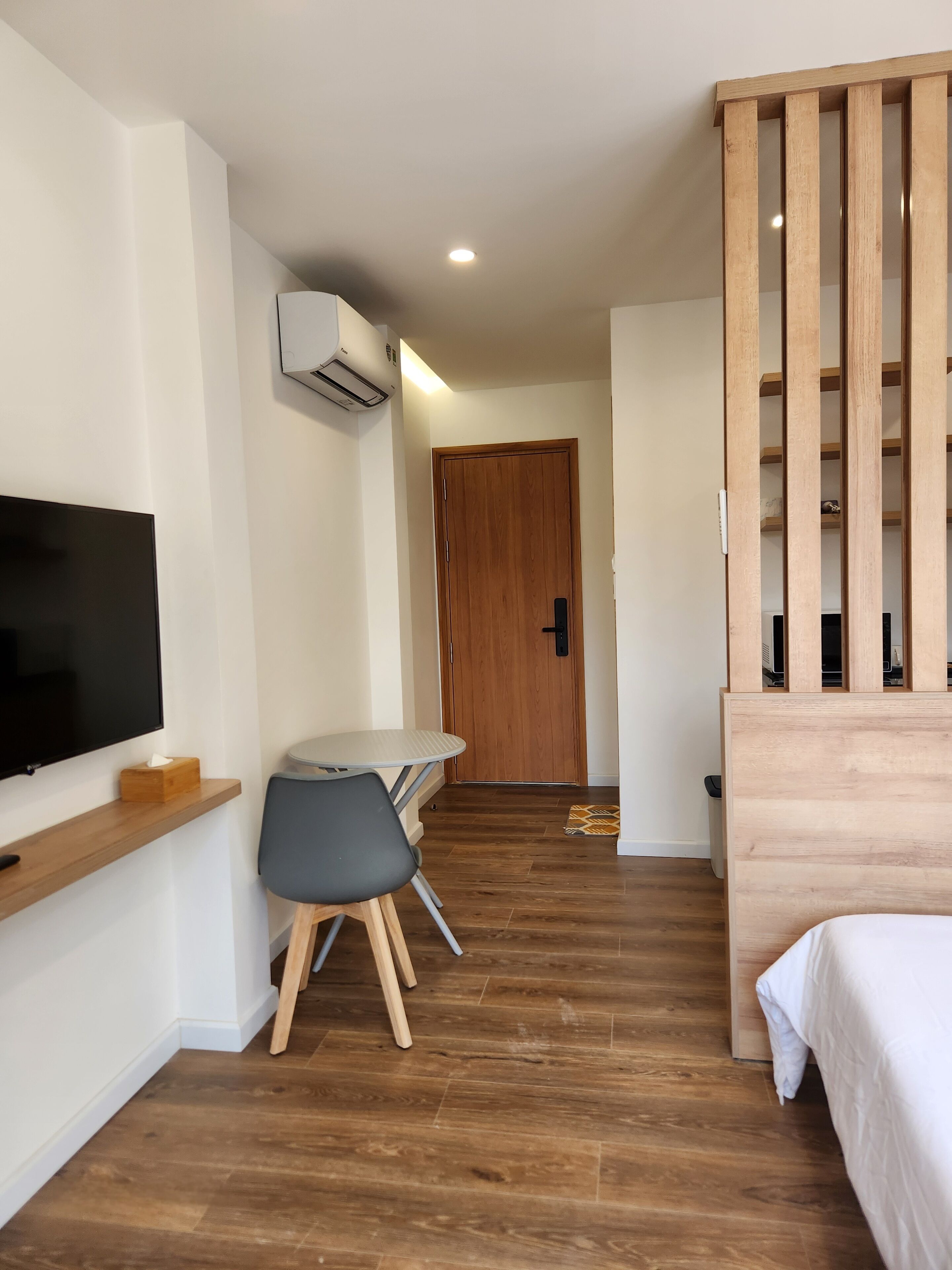 Una habitación de hotel moderna con piso de madera, una cama, un escritorio con silla, un televisor y un armario.