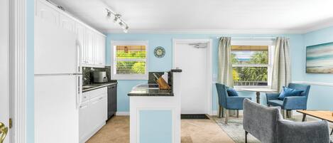 Una cocina compacta con armarios blancos, una isla central y una zona de comedor con sillas azules y una mesa.