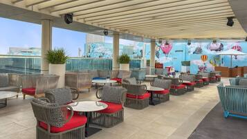 A rooftop bar with wicker furniture, red cushions, and a mural of hot air balloons.