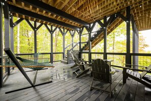 A covered outdoor deck with wooden railings, a hammock, and Adirondack chairs. - Multi-State Views|Hot Tub|Sleeps 14|Pets Welcome (Beech Mountain)