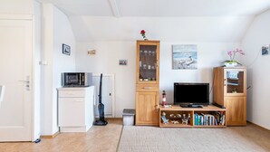 Ein Wohnzimmer mit Fernseher, Bücherregalen, einer Mikrowelle und einem Staubsauger.