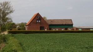 Ein aus roten Ziegeln gebauter Schuppen mit einem grünen Dach, umgeben von einem grünen Feld und einer Hecke.