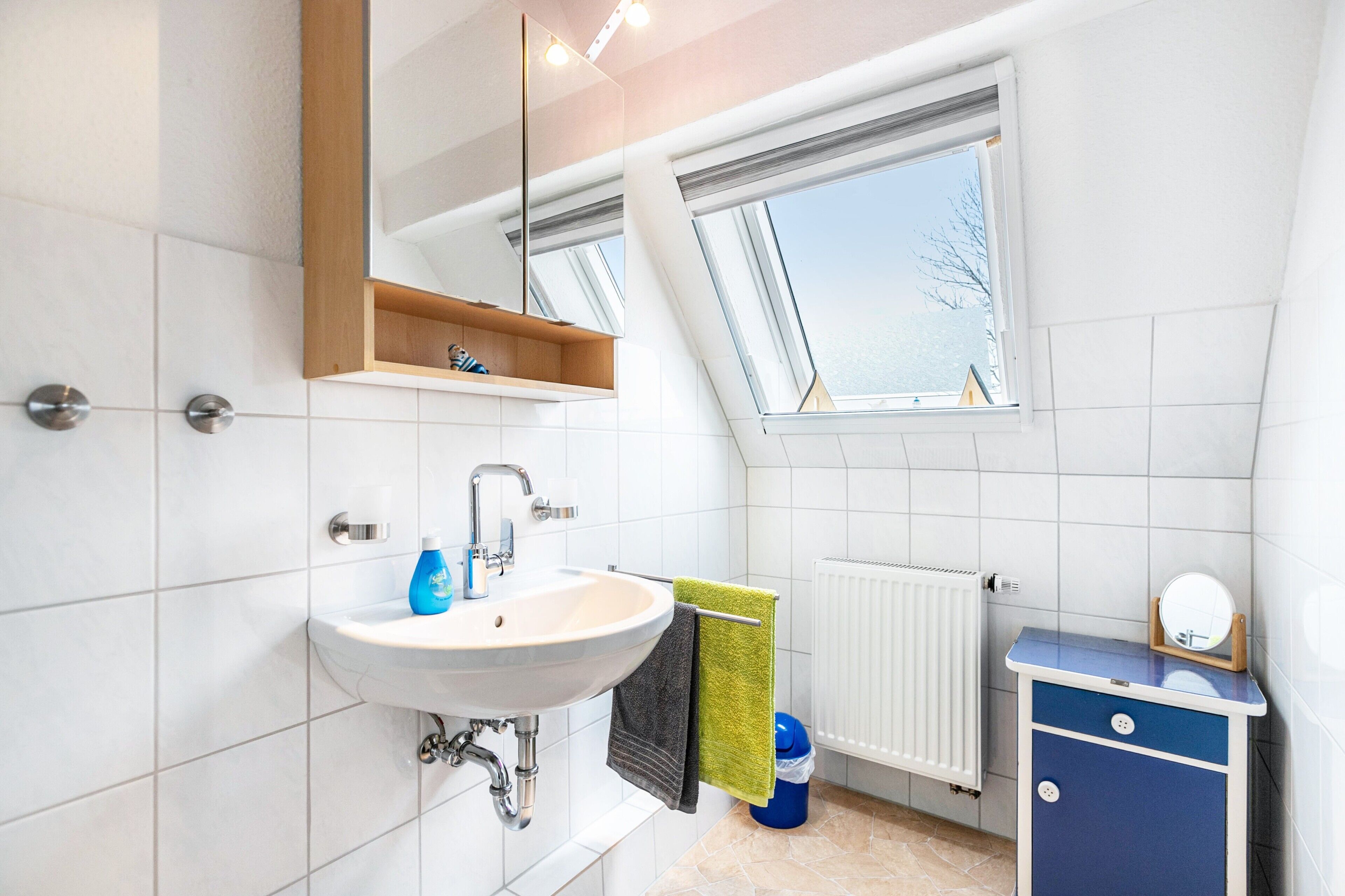 Ein modernes Badezimmer mit Oberlicht, Waschbecken, Spiegel und einem blauen Schrank.