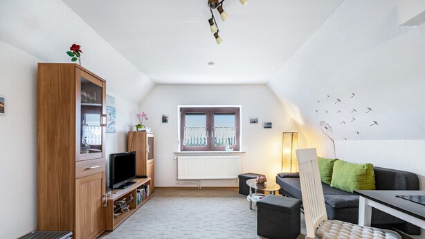 Ein gemütliches Wohnzimmer mit Fernseher, Holzschrank und Fenster mit Blick.