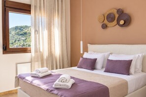 A hotel room with a bed, a view of a green landscape through a window, and a wall-mounted light fixture. - Cozy, family-friendly apartment with a view! (Skiathos)