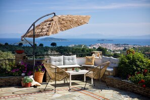 Eine Terrasse mit Blick auf das Meer, Korbmöbel und Topfpflanzen.