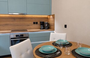 Eine moderne Küche mit Einbauofen, einer Kaffeemaschine und einem Essbereich mit Holztisch und weißen Stühlen.