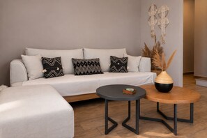 Ein modernes Wohnzimmer mit einem grauen Sofa, Kissen in Schwarz-Weiß-Muster, einem runden Couchtisch aus Holz und einem dekorativen Wandbehang aus Makramee.