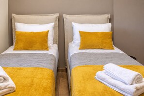 Zwei Einzelbetten mit weißer und senffarbener Bettwäsche, ein Holzboden und eine schlichte Wand.