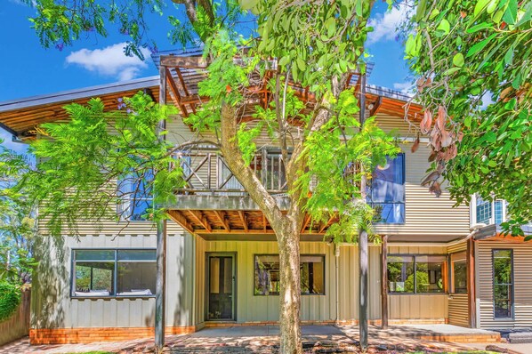 Une maison moderne à deux étages, dotée d’un patio couvert, de grandes fenêtres et d’un arbre dans le jardin.