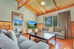 A spacious living room with a wooden ceiling, a large window with curtains, a flat-screen TV, and a sofa. - Echuca 265 - Your Rustic Retreat with Pool (Echuca)