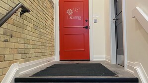 Una puerta roja con un logotipo, una barandilla negra y un felpudo negro que conduce a una escalera.
