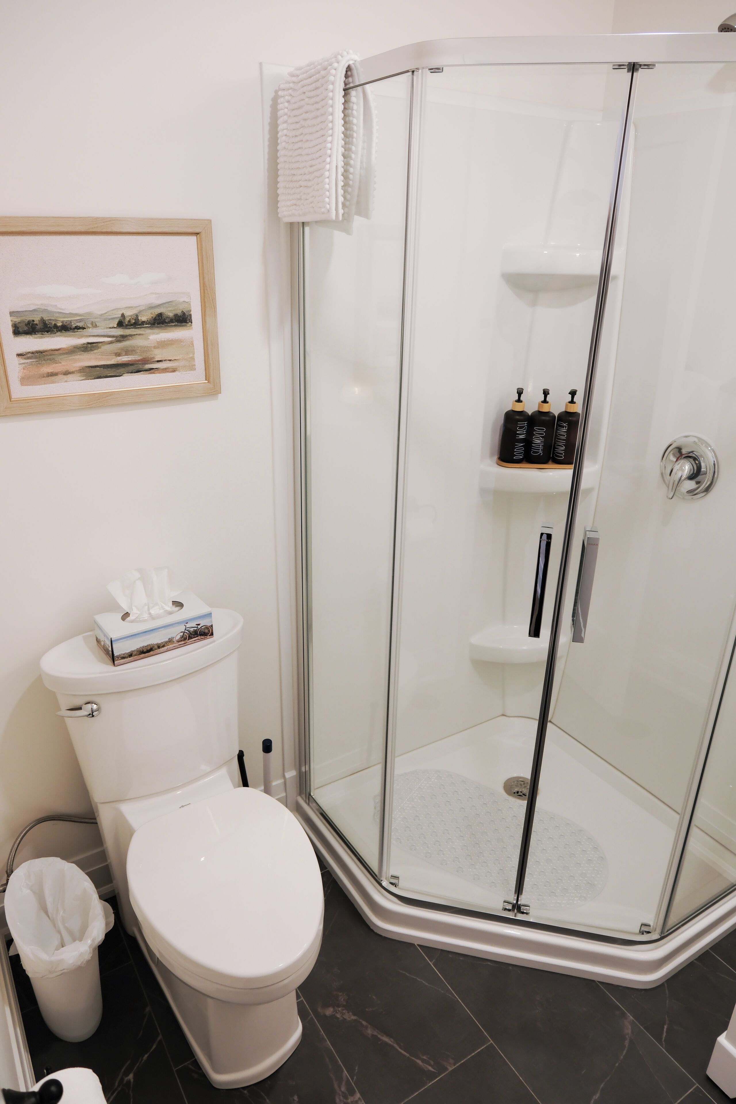 Een badkamer in hoekopstelling met toilet, een douchecabine en een plank met toiletartikelen.