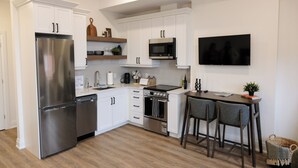 Una cocina moderna con gabinetes blancos, electrodomésticos de acero inoxidable, un microondas y un televisor de pantalla plana.