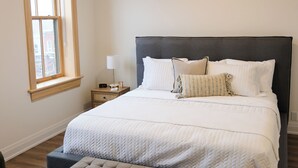 Un dormitorio con una cama grande, una mesita de noche con lámpara, un ventilador de techo y una ventana con persianas.