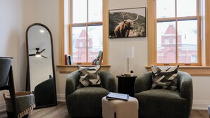 Una habitación con dos sillones, una lámpara de pie, un espejo y vistas a edificios a través de amplias ventanas.