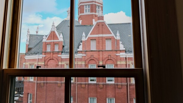 Vista a través de una ventana que muestra un edificio con una torre de reloj y fachada de ladrillo rojo.