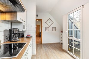 Eine moderne Küche mit Herd, Kaffeemaschine und Blick ins Freie durch ein großes Fenster.