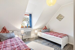 Ein Schlafzimmer mit zwei Betten, einem Heizkörper, einer Lampe und einem Fenster mit Vorhängen.