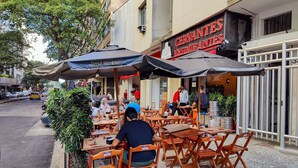 Ein Straßencafé mit Holztischen und -stühlen, Sonnenschirmen und im Hintergrund ein Restaurant namens "CERVANTES RESTAURANTE".