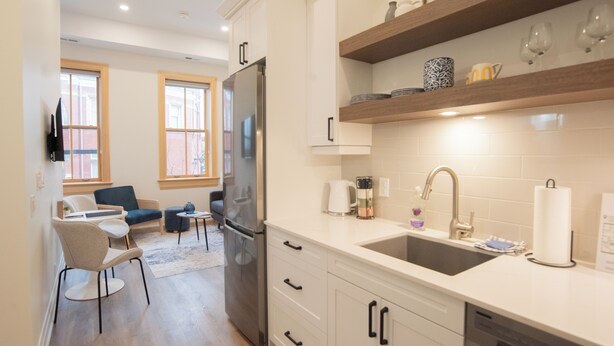 A modern kitchen with white cabinets, a stainless steel refrigerator, and a wooden shelf above the sink.