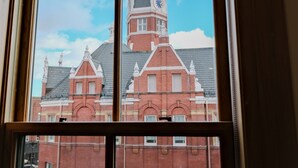A view through a window of a building with a clock tower and a red brick facade.