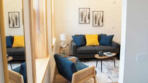A modern living room with a sofa, armchair, coffee table, and a large mirror.