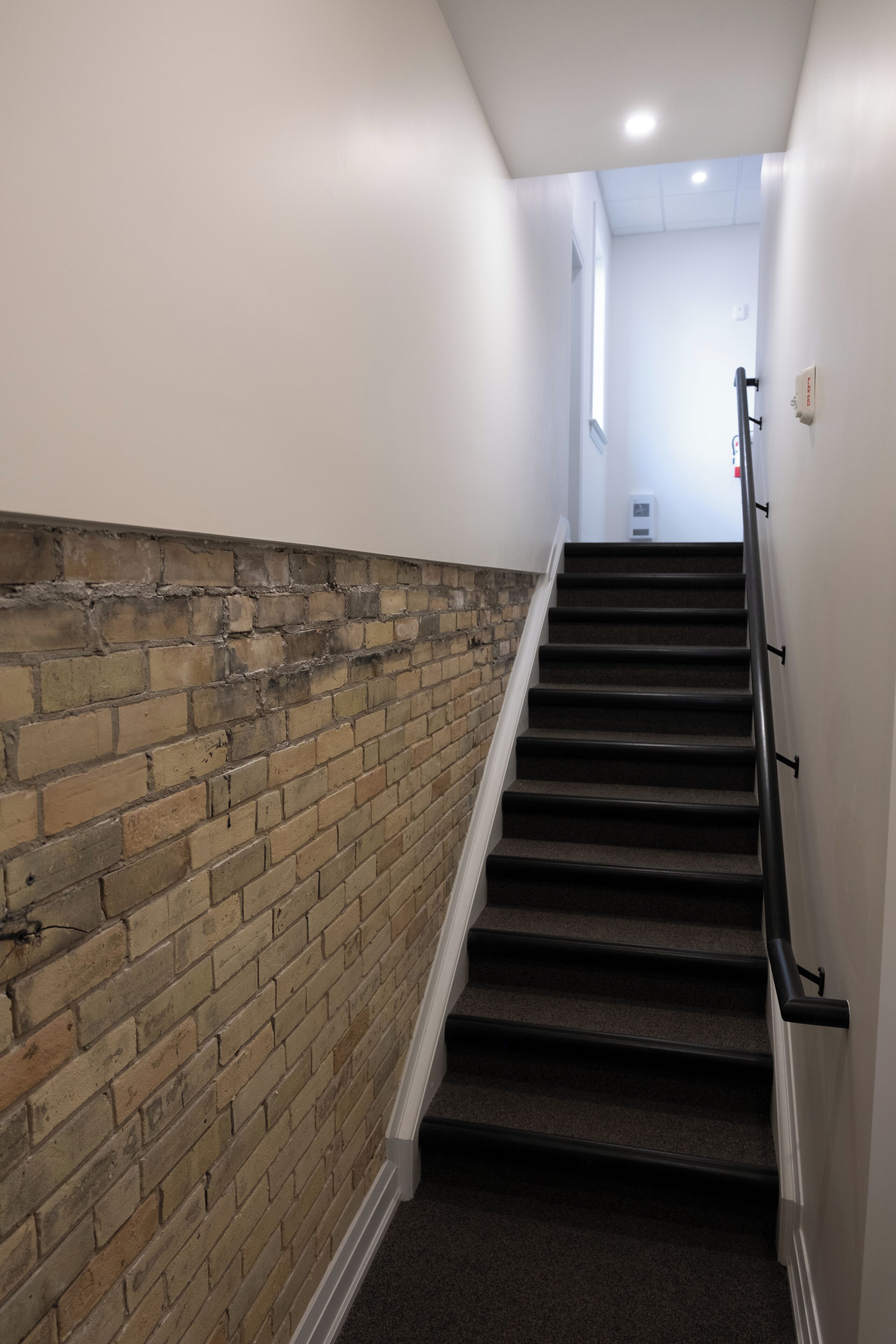 Eine Treppe mit einer Backsteinwand und einer weißen Wand, die zu einer Zwischenplattform mit einer Leuchte führt.