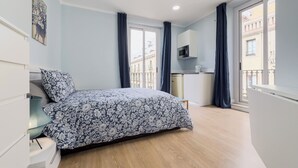 Ein Schlafzimmer mit Bett, Kommode, Mikrowelle und Blick auf die Stadt.