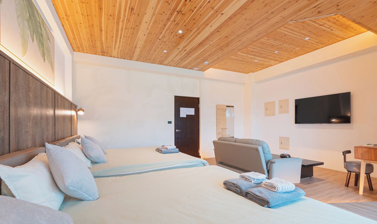 Una habitación de hotel moderna con dos camas, un escritorio, un televisor de pantalla plana y techo de madera.