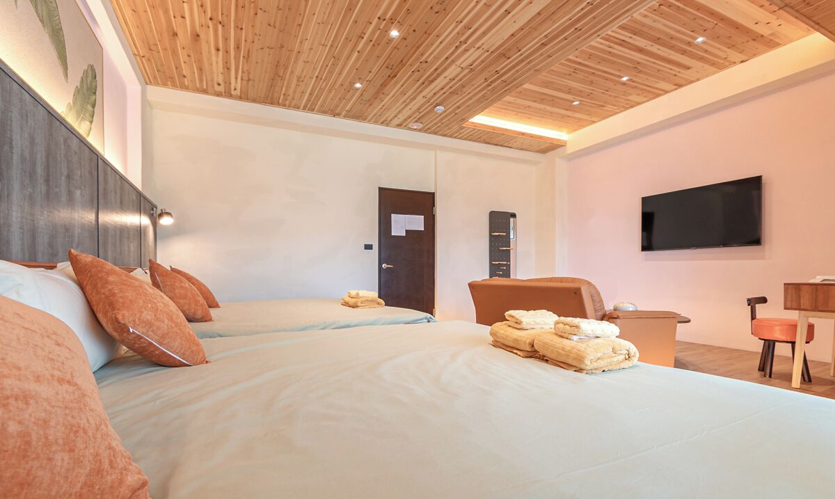 Ein Hotelzimmer mit zwei Betten, einem Flachbildfernseher, einer Holzbalkendecke und einem Schreibtisch mit Stuhl.