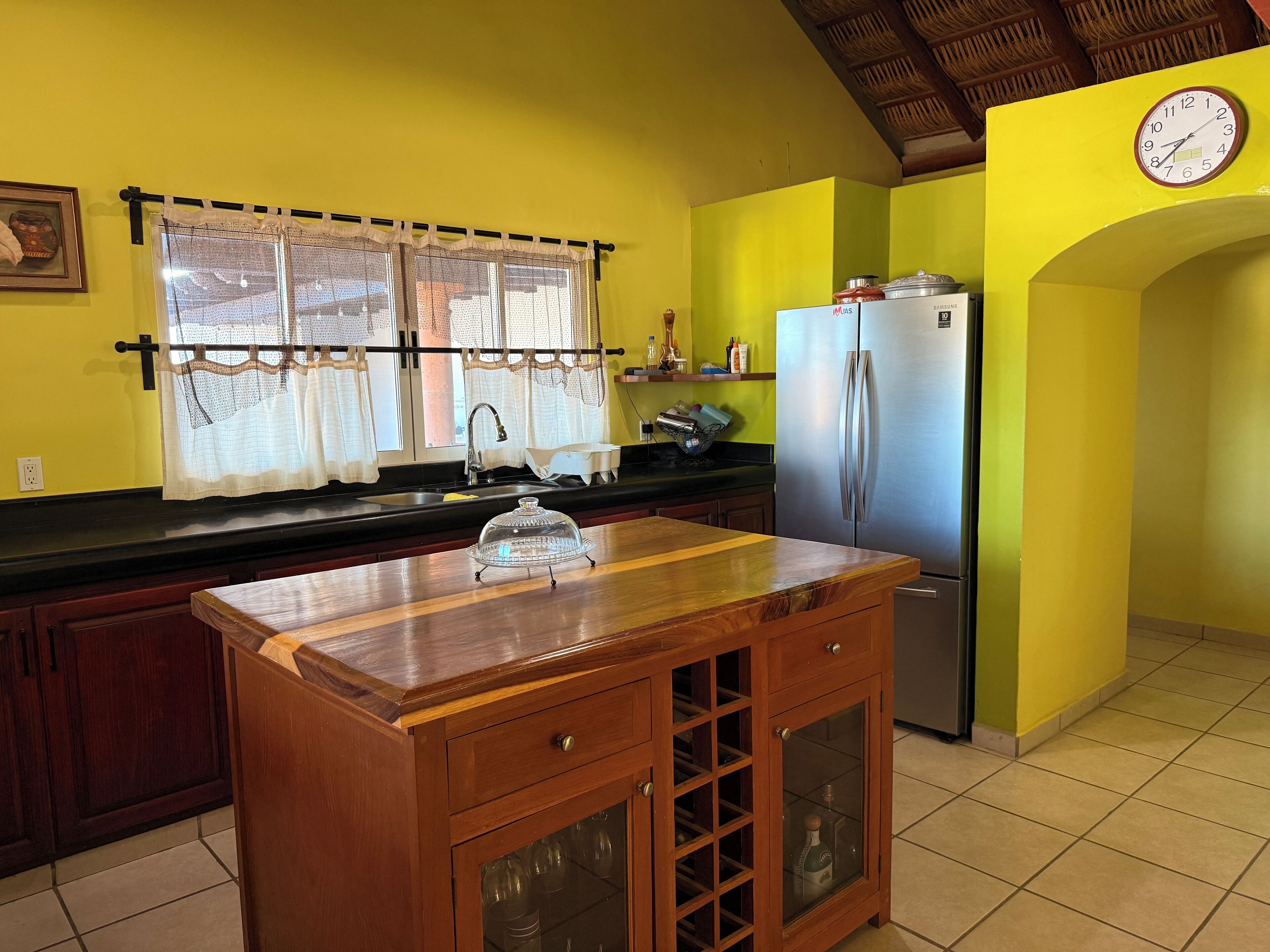 A kitchen with a wooden island, stainless steel refrigerator, and a clock on the wall.