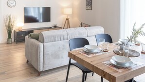 A modern living room with a sofa, a dining table set for four, a TV mounted on the wall, and a ceiling light fixture. - [Leopoldo Cozy Loft] Tram| Air C. | Smart TV (Firenze)
