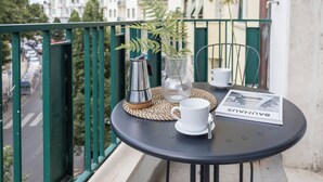 A balcony with a table set for two, featuring a white cup, saucer, a small vase with a plant, a metal coffee pot, and a magazine titled "BAUHUS". - [Leopoldo Cozy Loft] Tram| Air C. | Smart TV (Firenze)