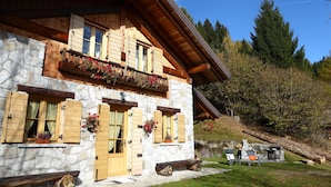 Un edificio de piedra con contraventanas de madera, un balcón con jardineras y una chimenea de piedra.