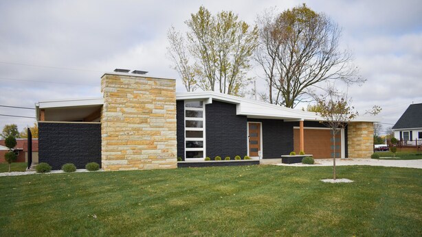 Une maison moderne à deux étages, dotée d’une façade en pierre, d’un garage et d’une pelouse bien entretenue.