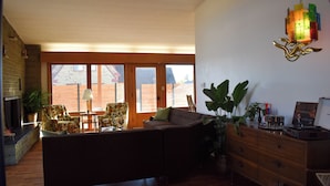 Un salon chaleureux avec une cheminée, un canapé et une table basse. Une grande fenêtre offre une vue sur un bâtiment en briques.