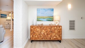 A wooden cabinet with geometric patterns, a landscape painting above it, and a lamp on the right. - War College Friendly Downtown Condo (Newport)