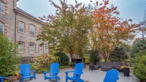 An outdoor seating area with blue Adirondack chairs and a concrete table, surrounded by trees and a stone building. - War College Friendly Downtown Condo (Newport)