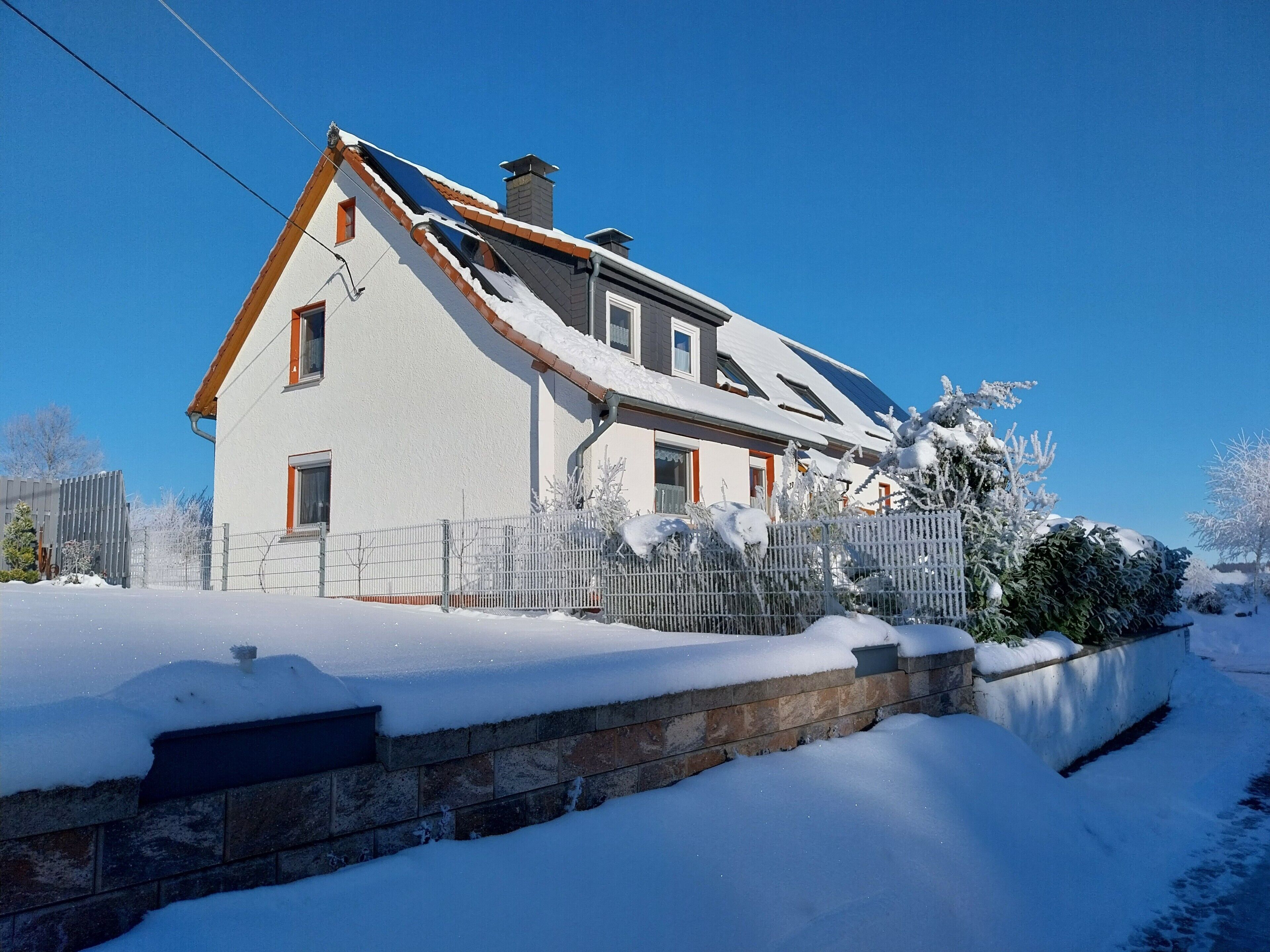 A two-story house with a sloped roof, a stone foundation, and a metal fence.